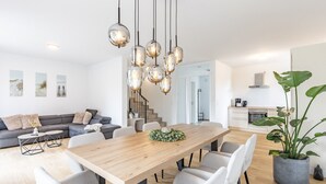 A modern kitchen with a built-in oven, a dining area with a wooden table and chairs, and a living area with a sofa and a coffee table. - Holiday Home 'Das Strandhaus 2' with Shared Terrace and Wi-Fi (Lembruch)