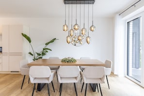 Un coin repas comprenant une table en bois, six chaises, un luminaire suspendu et une plante en pot.