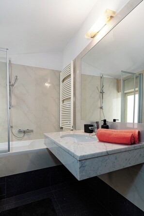 A modern bathroom with a marble vanity, a glass shower enclosure, and a large mirror.