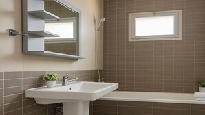 Une salle de bain avec un lavabo blanc, un miroir, une douche et une fenêtre.