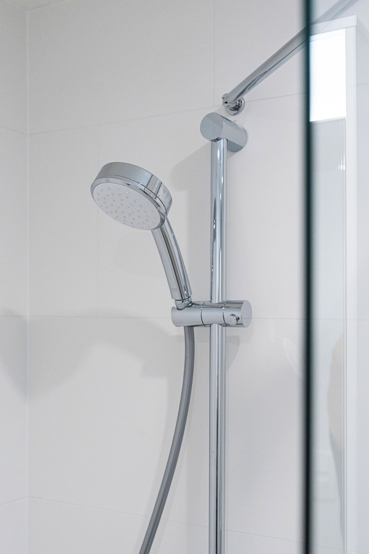 Une pomme de douche chromée au design incurvé, fixée sur un mur dont le fond est recouvert de carreaux blancs.