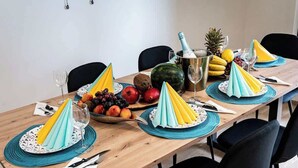 Et spisebord dækket med blå servietter, en skål med frugt, en champagneflaske og en vandmelon.