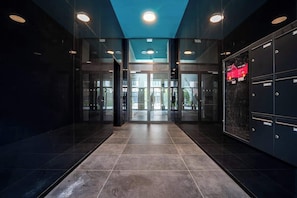 Un hall d’entrée moderne avec une entrée en verre, un sol carrelé foncé et un plafond bleu.