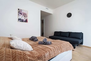 Une chambre à coucher avec un lit, un canapé noir, une horloge murale et une œuvre d’art florale encadrée.