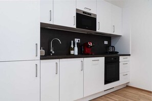 Une cuisine moderne avec des meubles blancs, un plan de travail noir, un four encastré, une machine à café et une bouteille de vin.