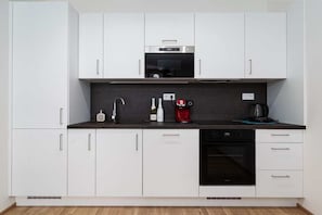 Una cocina moderna con armarios blancos, horno empotrado y cafetera.
