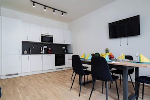 A modern kitchen with white cabinets, a black countertop, and a flat-screen TV mounted on the wall.