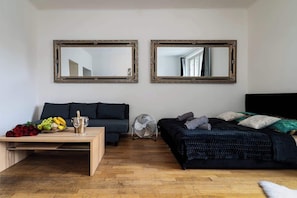 Una habitación con piso de madera, un sofá oscuro, una cama con manta estampada y dos espejos adosados a la pared.