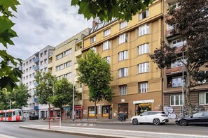 A multi-story residential building with balconies, a tram line, and parked cars.