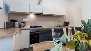 Una cocina moderna con armarios blancos, microondas, cafetera y una botella de vino en la encimera.