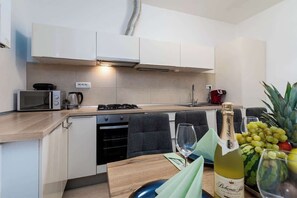 A modern kitchen with white cabinets, a microwave, a coffee maker, and a wine bottle on the counter. - Royal Aurora Residence (Prague 7)