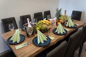 A wooden dining table set with plates, napkins, cutlery, and a bottle of champagne.
