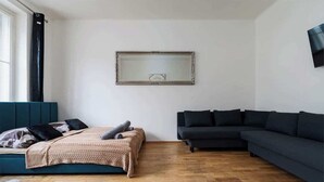 Una sala moderna con una cama, un sofá oscuro y un espejo grande en la pared.
