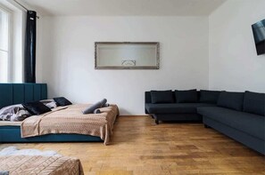 A modern living room with a bed, a dark sofa, and a large mirror on the wall. - Royal Aurora Residence (Prague 7)