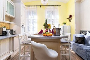 Una cocina compacta con armarios blancos, una zona de comedor con una silla blanca y un sofá azul.