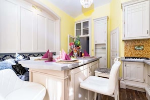 A kitchen with white cabinets, a central island with a sink, and a dining area with a chair and table. - Imperial Deluxe Suite (Prague)