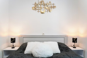 A bedroom with a bed, two bedside lamps, a wall art piece, and a white headboard.