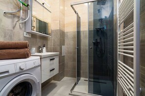 A modern bathroom with a glass shower enclosure, a washing machine, and a towel rack.