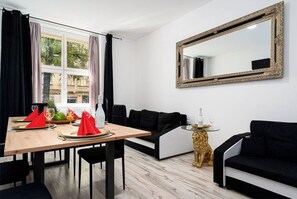A modern living room with a dining area, featuring a large mirror, black sofas, and a wooden dining table set with red napkins and glasses. - Lion Deluxe Suite (Praha 2)