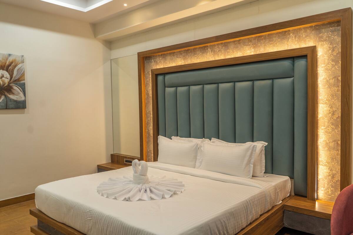 A neatly made bed with a headboard, a wall-mounted painting, and a bedside table.