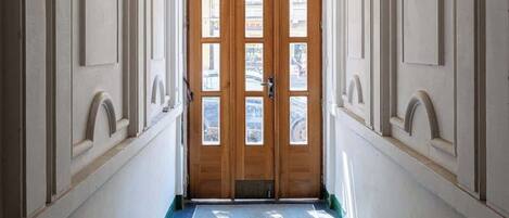 A hallway with a double wooden door, white walls, and a ceiling light.