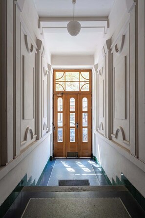 Un couloir avec une porte double en bois, des murs blancs et un luminaire au plafond.