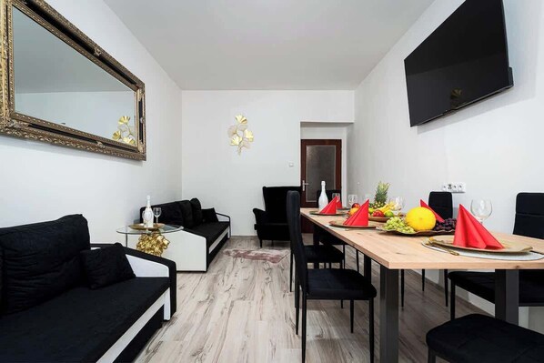 Un espace repas moderne avec une table en bois prévue pour quatre personnes, des chaises noires à revêtement en tissu et un canapé noir.