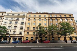 A multi-story building with a yellow facade, multiple windows, and a pedestrian area with parked cars. - Lion Deluxe Suite (Praha 2)
