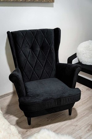Un fauteuil noir, recouvert de tissu, avec un dossier matelassé, placé sur un plancher en bois et agrémenté d’un tapis blanc.