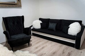 Un canapé noir avec des coussins blancs et moelleux, un fauteuil noir et un tapis blanc à poils longs.
