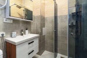 A modern bathroom with a glass shower enclosure, a white vanity with drawers, and a mirror above the sink. - Lion Deluxe Suite (Praha 2)