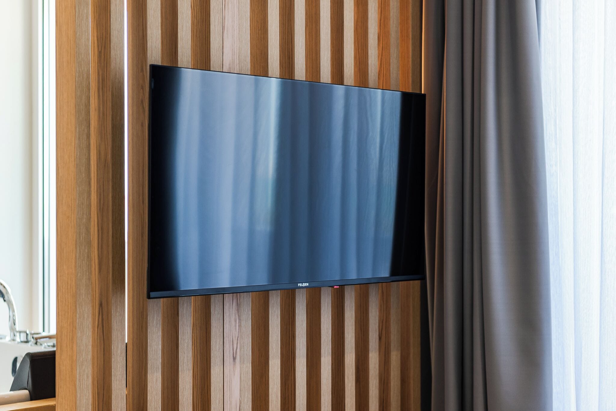 A flat-screen TV mounted on a wooden wall with vertical stripes.