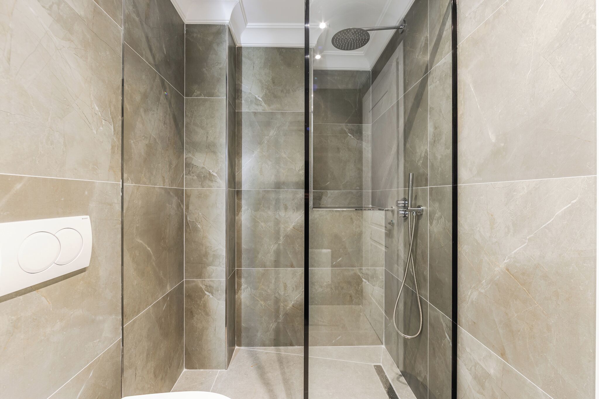 Une douche moderne dotée d’une porte en verre, d’un pommeau de douche à main et d’un panneau de commande fixé au mur.