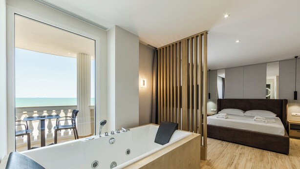 A modern bedroom with a large bathtub, a bed with neatly made linens, and a view of the ocean through a balcony. - SEA LA VIE SUITES (Golem)