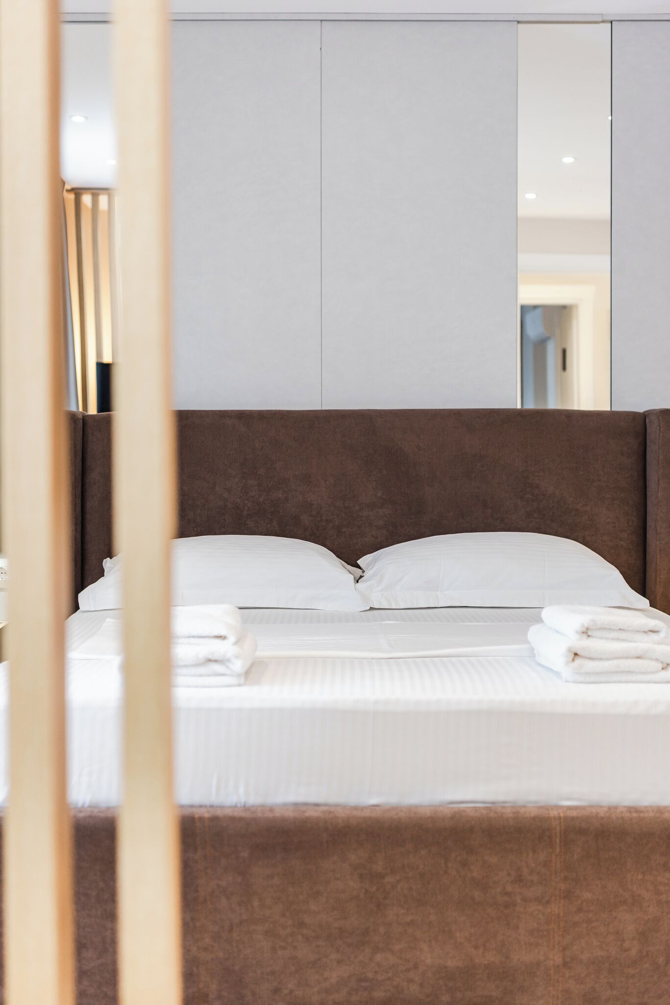 Una cama bien hecha con sábanas y almohadas blancas, un cabecero marrón y un espejo grande sobre la cama.