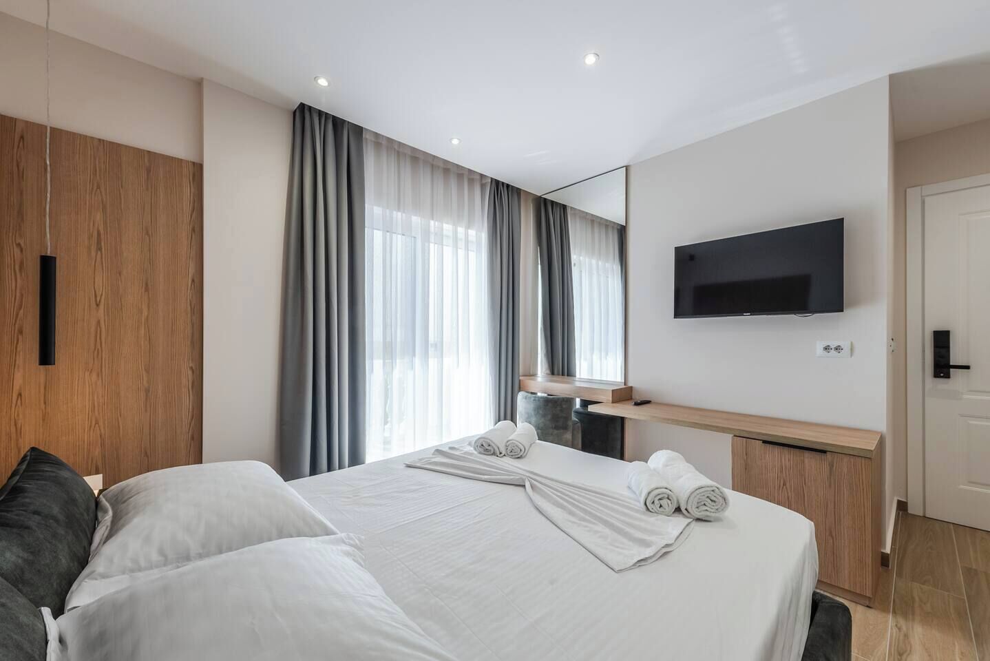 Una habitación de hotel moderna con una cama grande, un televisor de pantalla plana en la pared y un armario de madera.