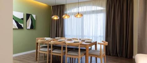 A dining area with a wooden table and chairs, a modern pendant light fixture, and a large window with curtains.