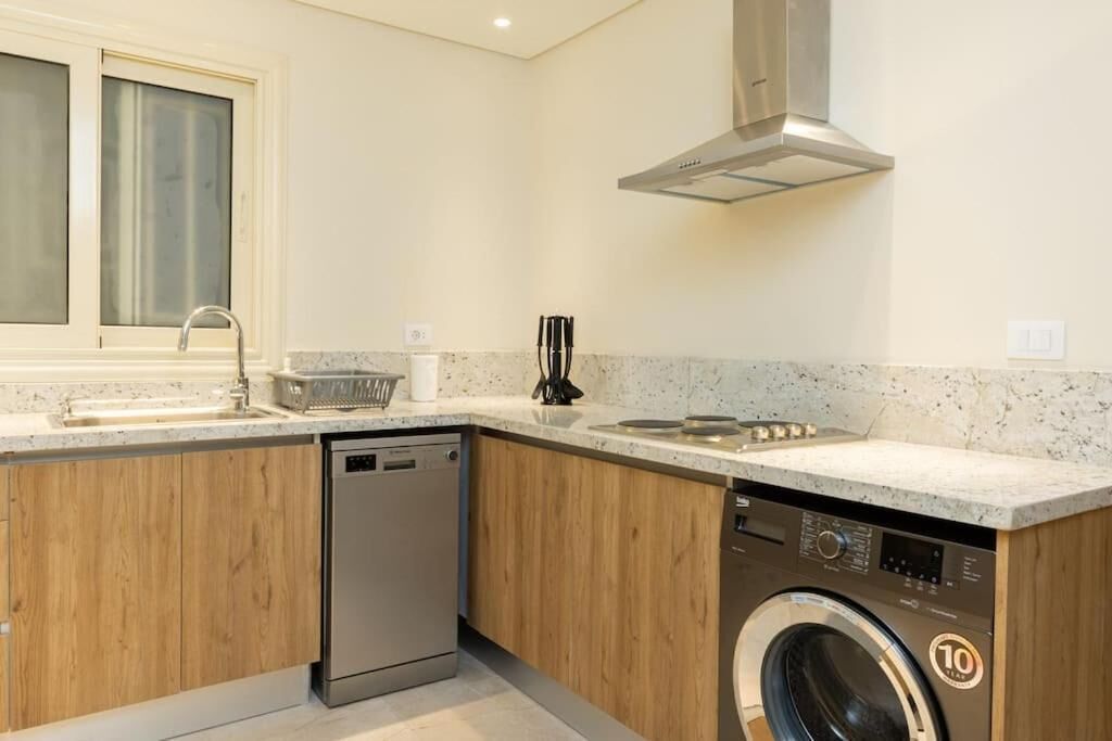 A compact kitchen with a dishwasher, washing machine, and a window with frosted glass.