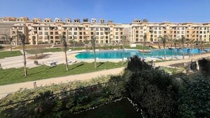 A multi-story hotel with a pool area, including a large central pool and a smaller adjacent pool. - Kennah Meraviglia | 4BR Stone Residence, New Cairo - Families Only (New Cairo)