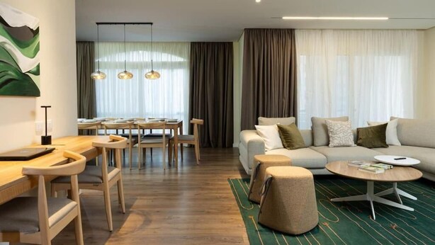A modern hotel room with a wooden dining table, chairs, a sofa set, and a round coffee table. - Kennah Meraviglia | 4BR Stone Residence, New Cairo - Families Only (New Cairo)