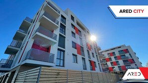 A modern multi-story building with balconies, a wooden fence in front, and the sun shining.