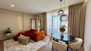 A modern living room with a sofa, a dining table with chairs, a coffee table, and a potted plant.