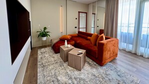 A modern living room with a large flat-screen TV, a red sofa, a coffee table, and a potted plant.