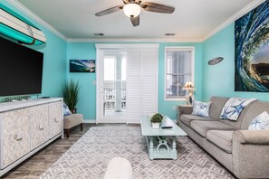 A living room with a ceiling fan, a flat-screen TV, a sofa, a coffee table, and a patterned rug.