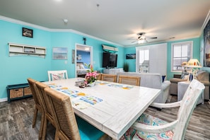 Uma sala de jantar ampla com uma mesa branca, cadeiras de vime e vista para a praia.