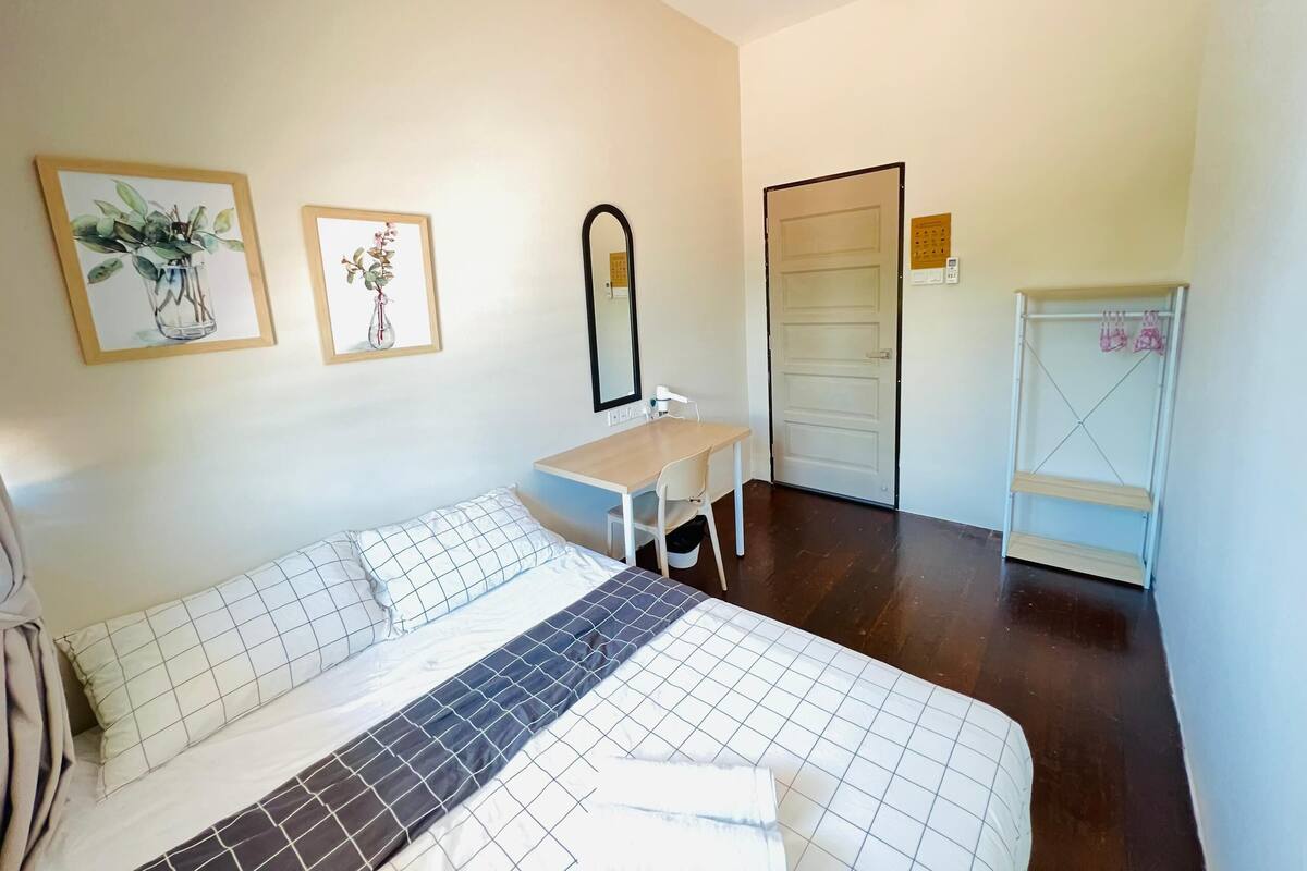 A bedroom with a bed, a desk, a chair, a mirror, and a door.