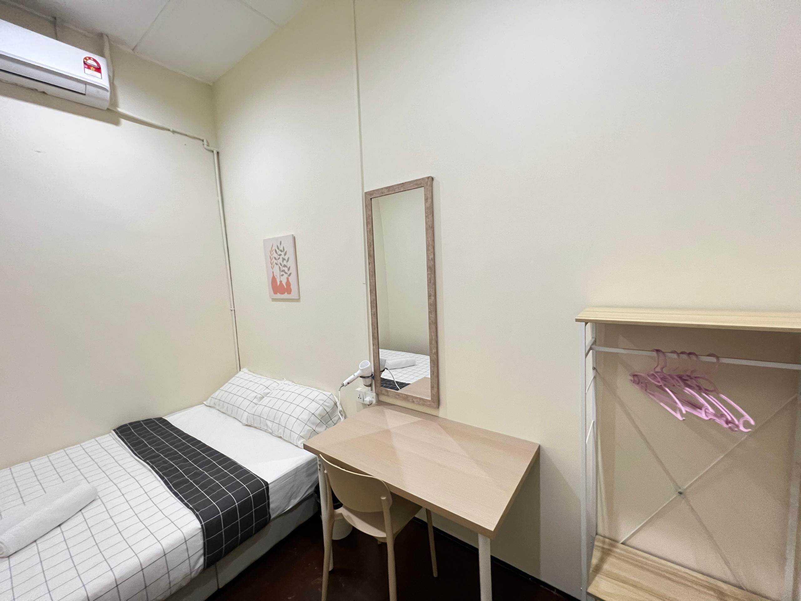 A small, simple room with a bed, a desk, a mirror, and a hanging clothes rack.