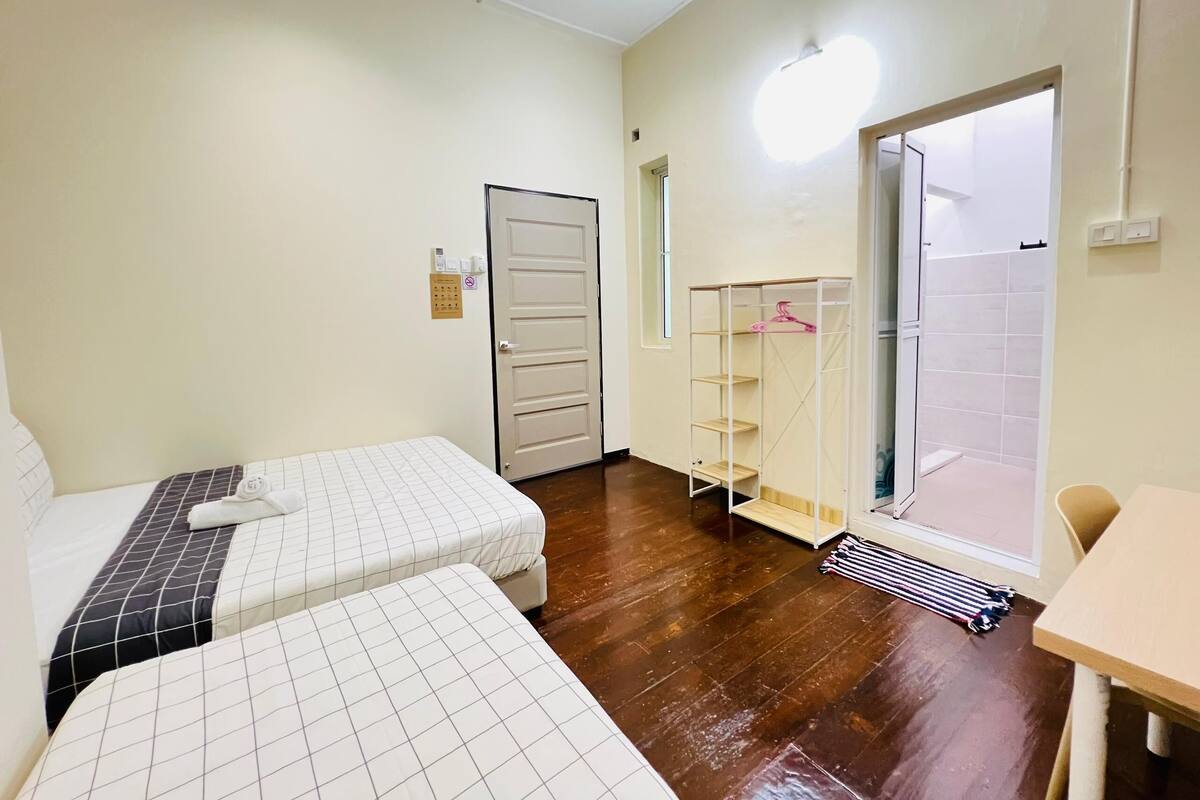 A hotel room with two beds, a wardrobe, a bathroom with a shower, and a small table.