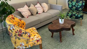 A living room with a sofa, floral armchair, coffee table, and a plant. There are three botanical prints on the wall. - myRoom at 14 J Mandalay (George Town)