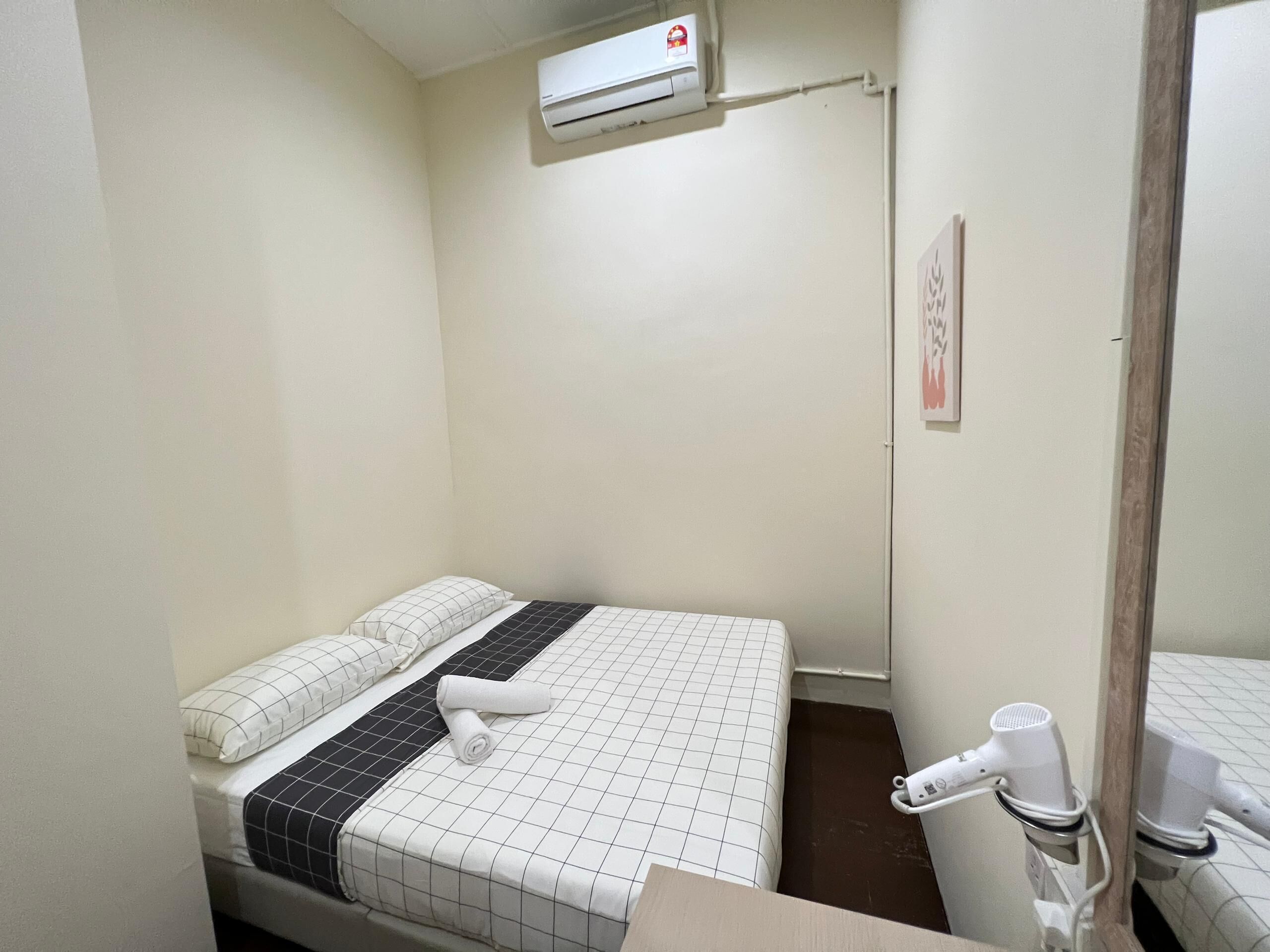 Une petite chambre propre, équipée d’un lit, d’une serviette, d’un climatiseur et d’un sèche-cheveux.
